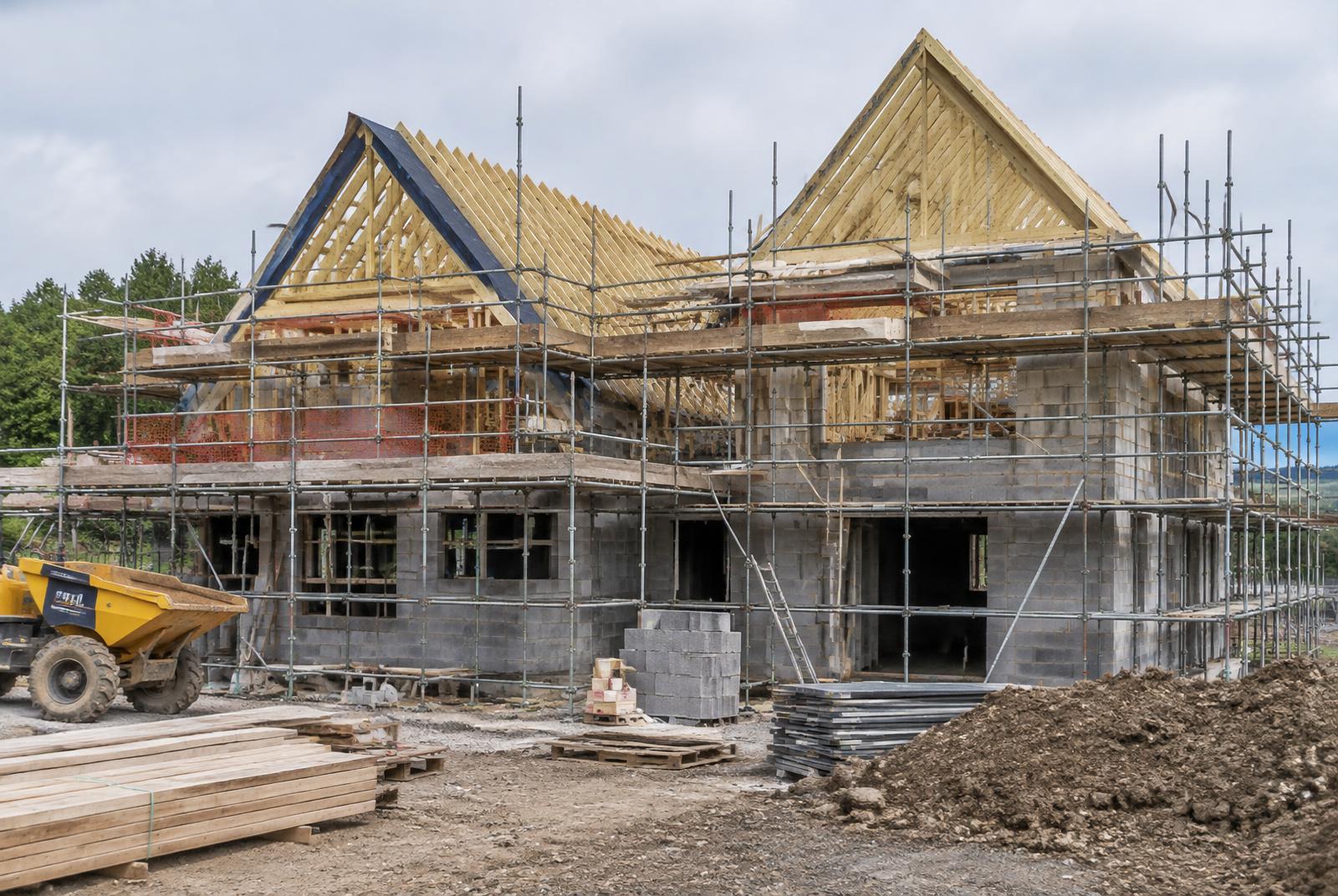 New build detached house under construction with blockwork walls, timber roof trusses and scaffolding